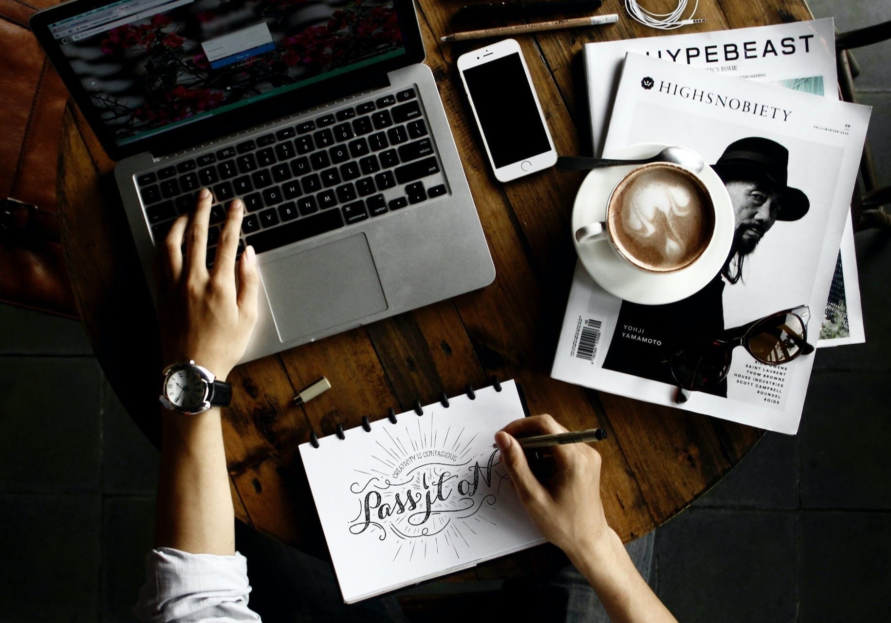 Man typing on a laptop while sketching on notebook paper
